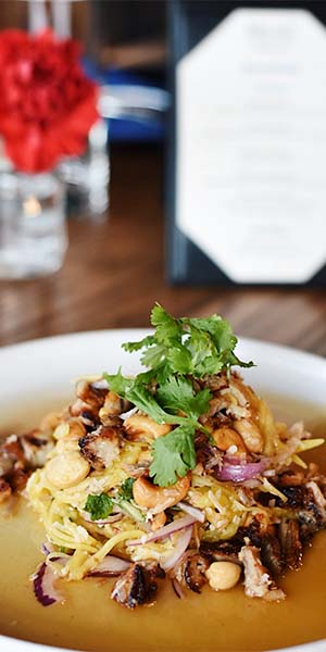 A bowl of Tom Yum Pasta: spaghetti in a Tom Yum inspired sauce with red cherry tomatoes and shrimp, topped with bright green curls of green onion.